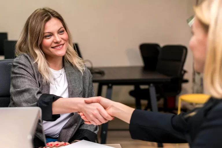 Bireysel emeklilik aktarım (taşıma) işlemini ve şirket değişikliği anlaşmasını simgeleyen, ofiste el sıkışan iki iş kadını.