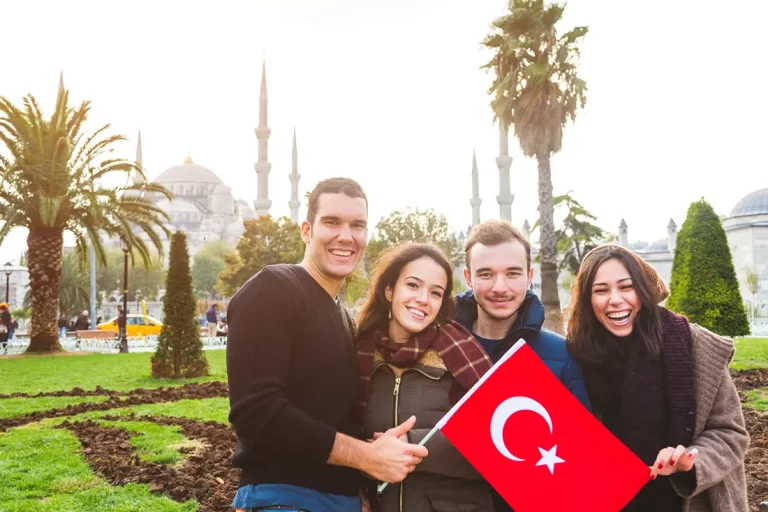 İstanbul'da bir cami önünde gülümseyerek Türk bayrağı tutan yabancı uyruklu gençler.