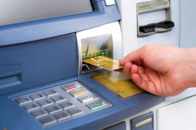 ATM cihazına altın renkli bir banka kartı yerleştiren el.
